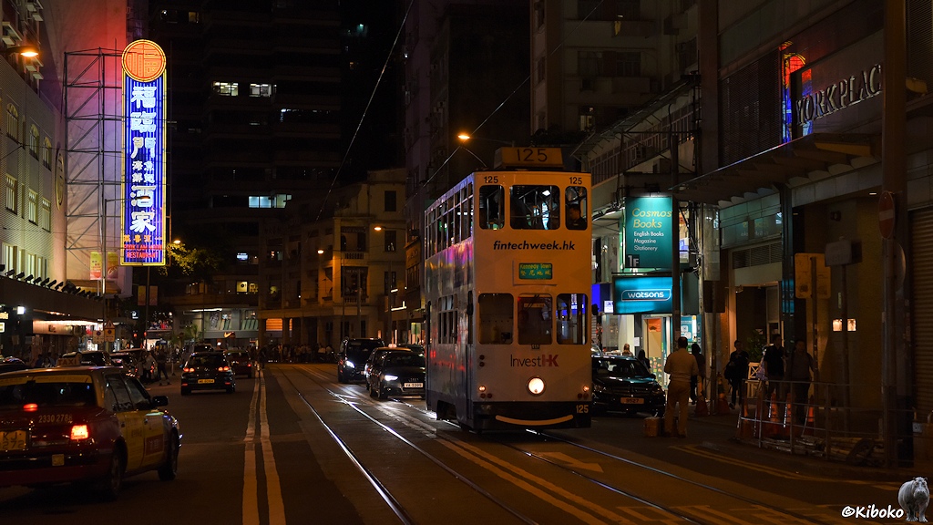 Das Bild zeigt eine Nachtaufnahme der weiß-hellblauen Tram 125 in einer Geschäftstraße mit Leuchtreklamen mit chinesischen Schriftzeichen.