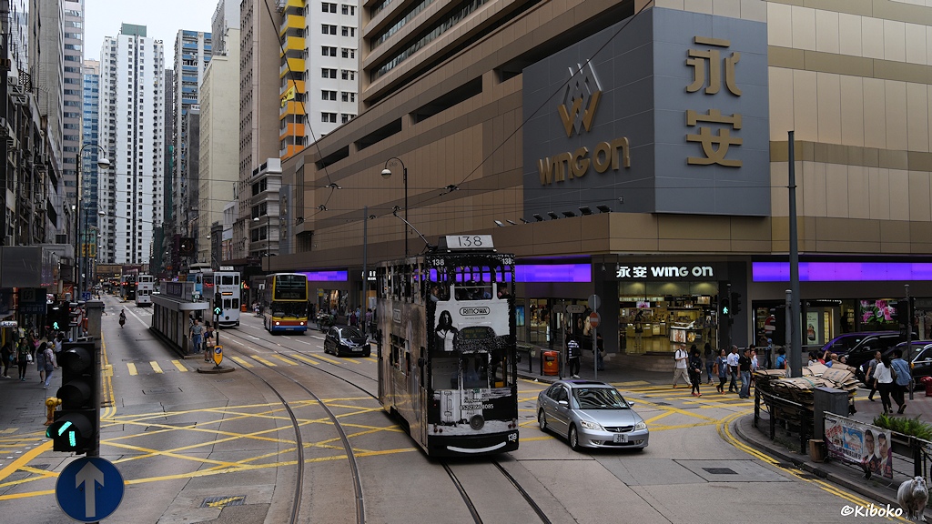 Das Bild zeigt die schwarz-weiße Tram mit der Nummer 138 auf einer Kruezung im Bogen. Im Hintergrund ist ein beigefarbenes Geschäftshaus mit einem umlaufenden violetten Leuchtband. Im Hintergrund sind Hochhäuser mit 38 Etagen.