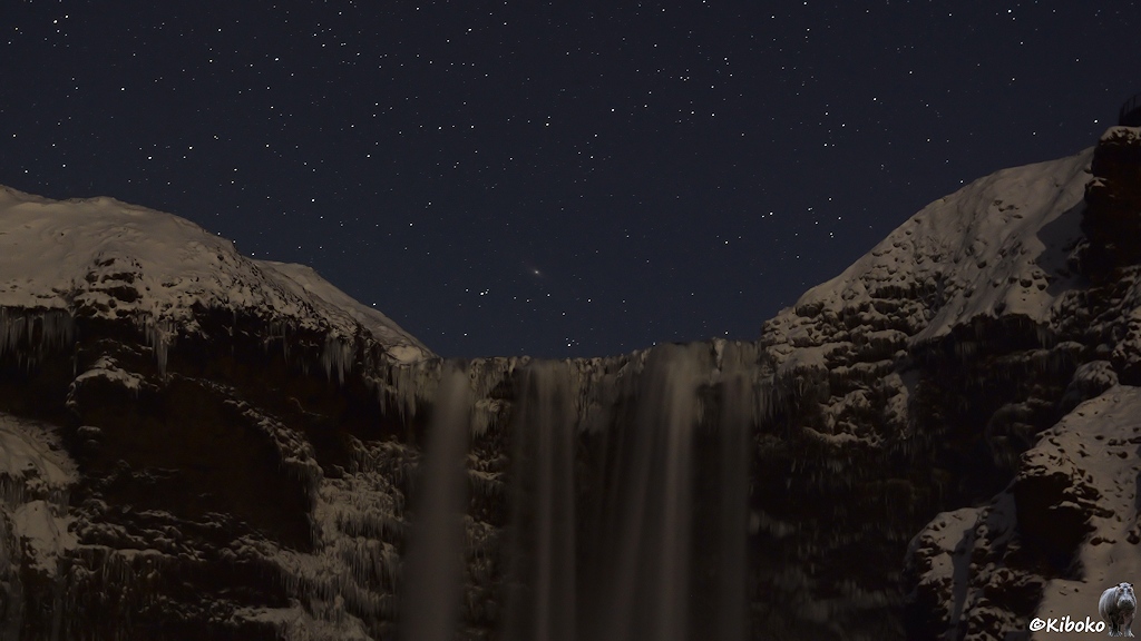Das Bild zeigt eine Detailansicht der Kante über der das Wasser fällt. Daneben sind dunkler Fels, teils schneebedeckter Fels. Darüber leuchten die Sterne.