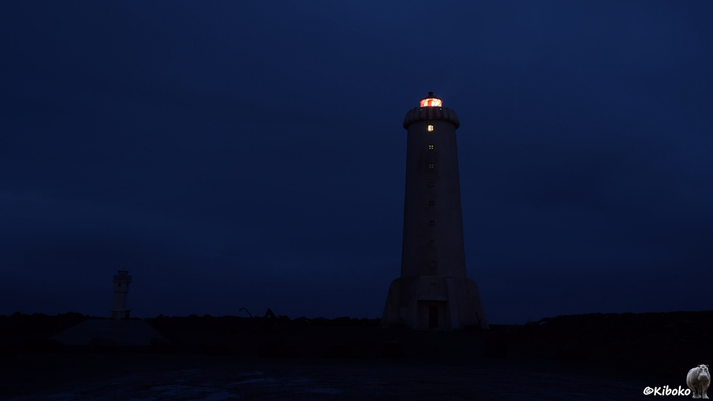 Die Silhouette eines Leuchtturms steht vor einem dunkelblauen Himmel in der Morgendämmerung. Das Licht im Leuchtturm ist sichtbar.
