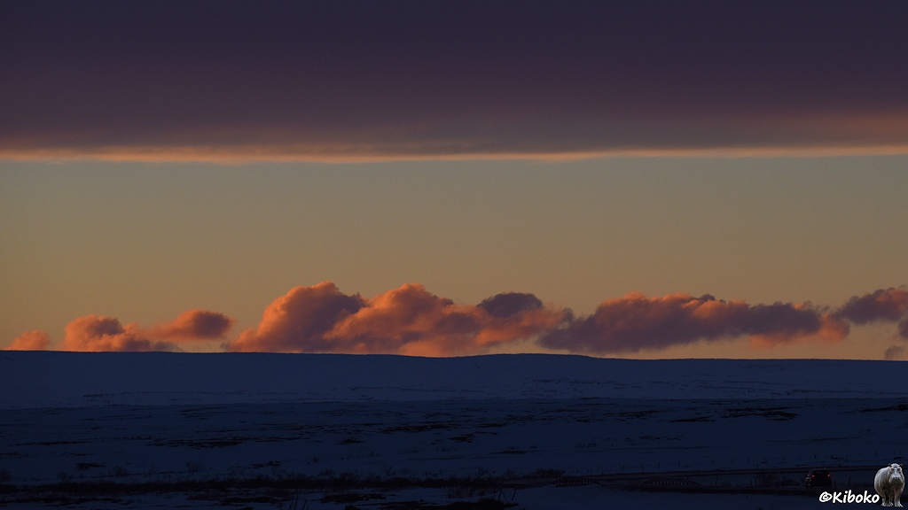 Zwischen dunkler Landschaft und dem Ende einer dunklen Wolkendecke ist eine Wolkenlücke am Horizont. Einzelne Wolken werden darin von der Sonne von unten orange angestrahlt.