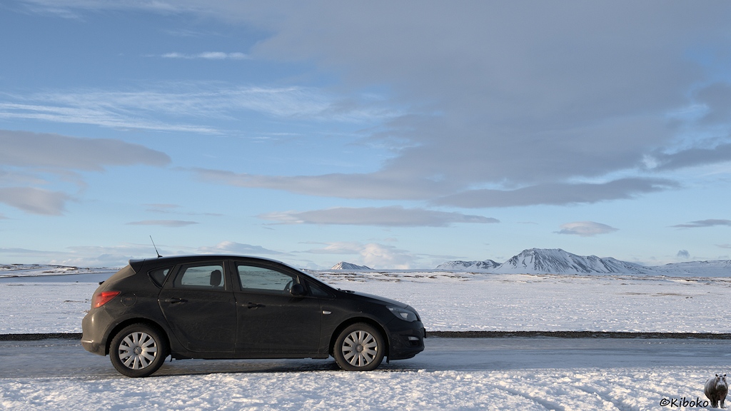 Seitenansicht eines schwarzen, viertürigen Autos mit Fließheck auf einer vereisten Straße. Im Hintergrund ist eine Schneefläche und Berge.