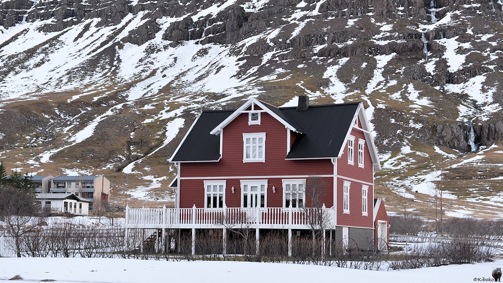 Rotbraunes Holzhaus mit schwarzem Dach und weißen Fenstern