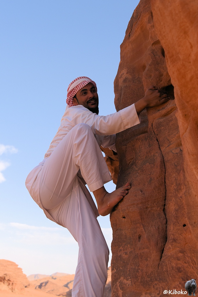 Ein Beduine in weißem Gewand klettert auf einen Felsen
