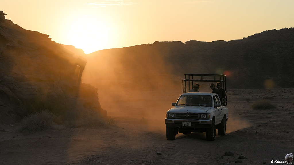 Weißer Geländewagen vor schwarzen Felsen in einer Staubwolke gegen die Sonne fotografiert