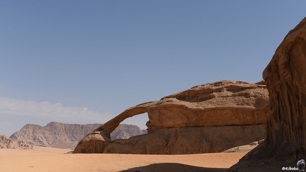 Weißer Geländewagen in ornageroter Wüste vor Bergkulisse mit wolkenverhangenen Himmel