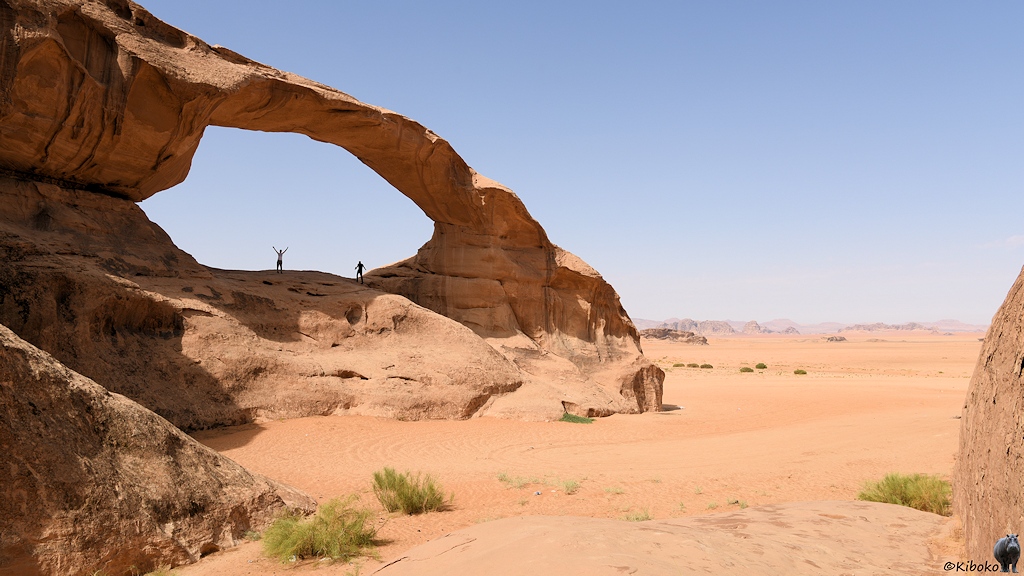 Felsvorsprung mit Bogen und zwei kleine Menschen in einer endlosen Wüstenlandschaft