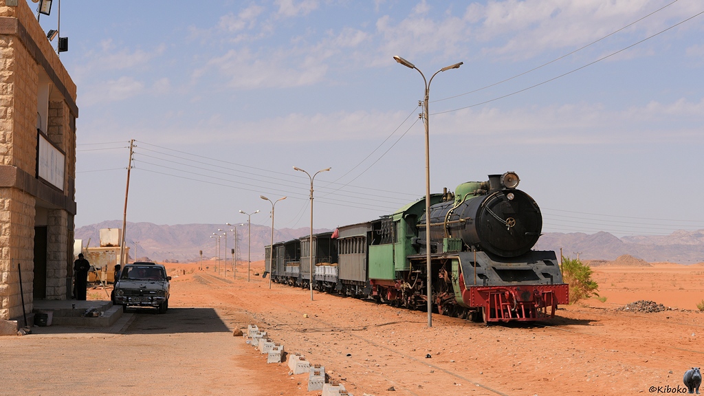 Eine grün-schwarze Dampflok mit rotem Fahrwerk vor Touristenzug mit 4 Personen- und zwei Flachwagen