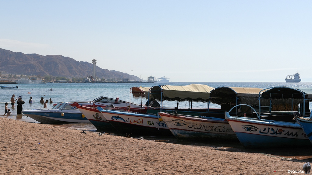 Menschen und Boote am Strand mit Hafenanlagen im Hintergrund