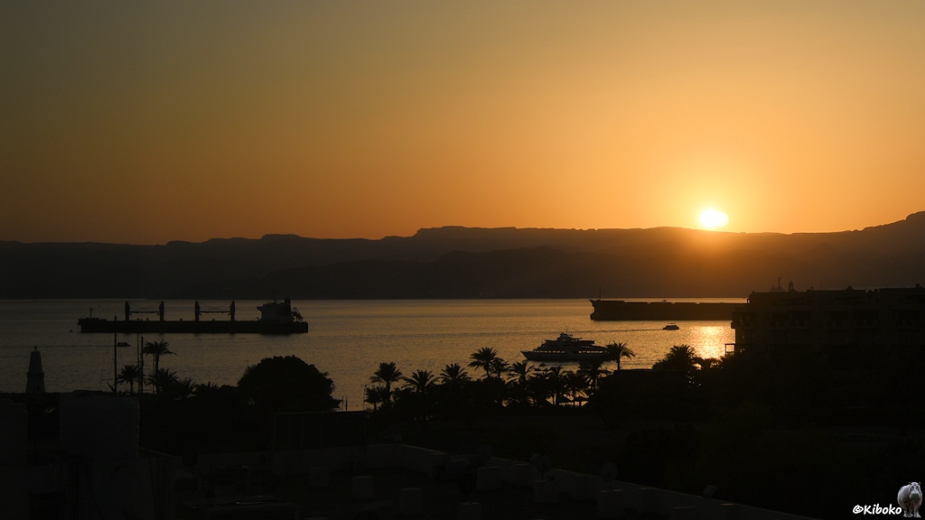 Die Sonne geht hinter einen Hafen mit Schiffen und einer Bergkette unter
