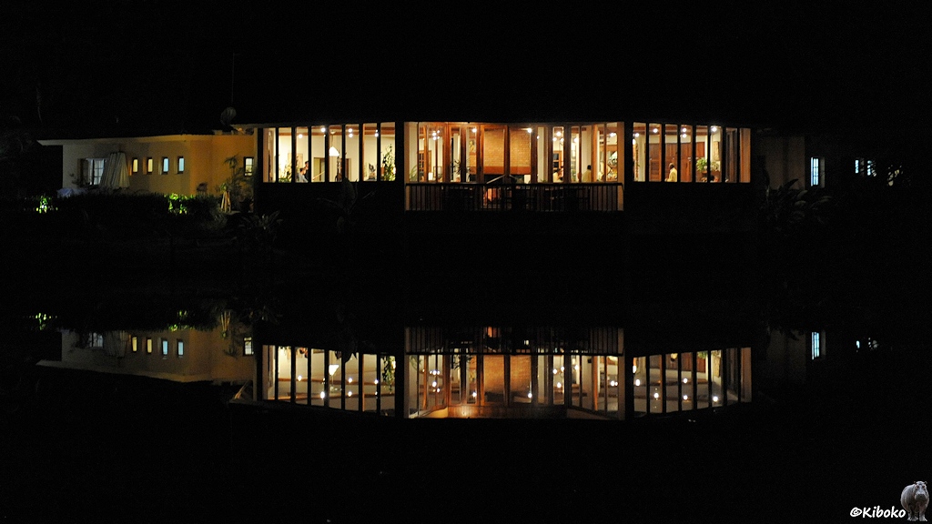 Im dunkeln spiegeln sich die Lichter eines Gebäudes in einem See.
