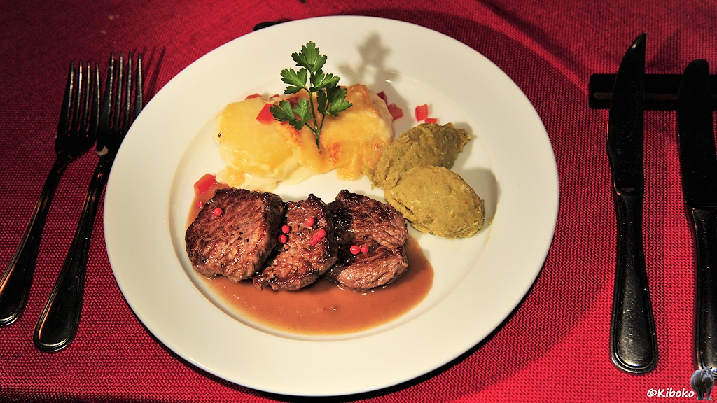Das Bild zeigt einen Teller mit drei Fleischbrocken, zwei Kleckse mit pürierten Erbsen und zwei Kartoffeln mit etwas Petersilie dekoriert.
