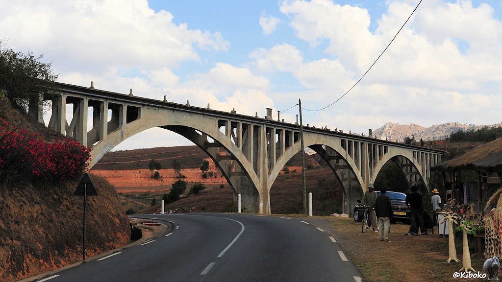 Eine Bahnlinie überquert die Straße und ein Tal mit einer filigranen Bogenbrücke aus Beton.