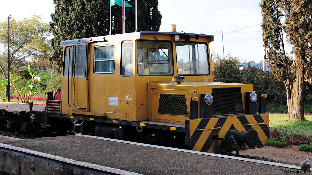 Ein kleines, gelbes, zweiachsiges Schienenfahrzeug mit niedrigen Motorvorbau steht an einem Bahnsteig.