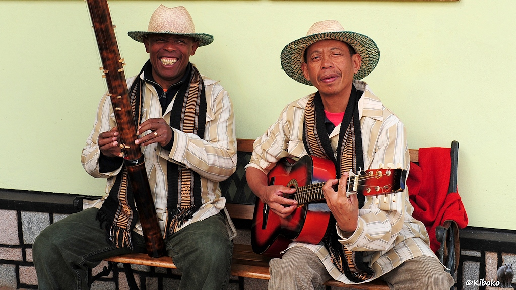 Das Bild zeigt zwei Musiker mit weißbraunen Jacken, schwarz-goldenen Schals und Strohüten. Einer spielt Gitrarre der zweite spielt ein sehr langess Seiteninstrument.
