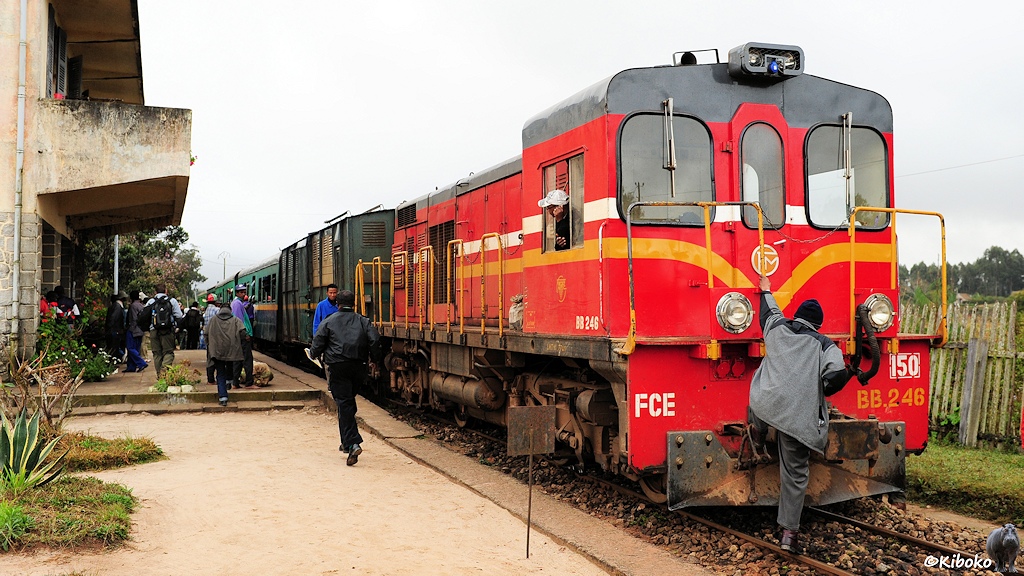 Das Bild zeigt einen Mann in grauen Arbeitsanzug, der auf die vordere Kupplung einer roten Diesellokomotive steigt.