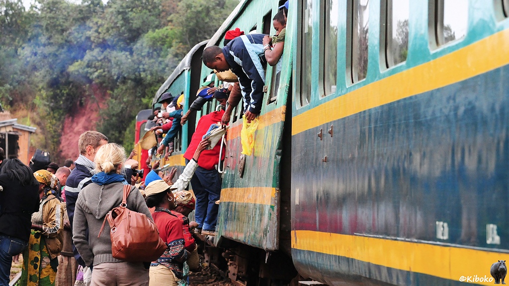 Das Bild zeigt Reisende, die sich weit aus dem Zugfenster lehnen und die Arme ausstrecken. Frauen mit Körben reichen ihre Waren in die Höhe.