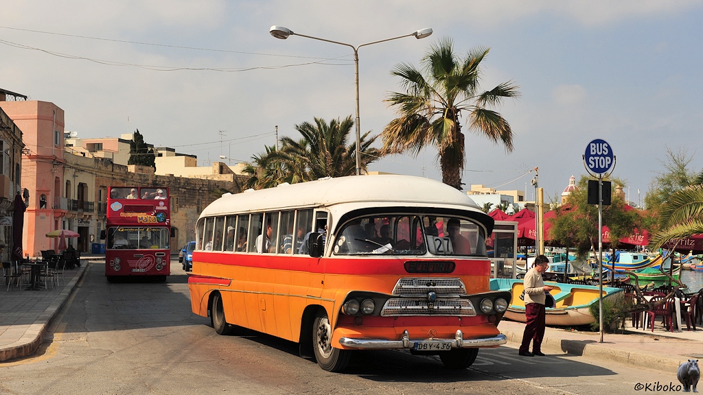 Das Bild zeigt einen alten rundlichen Bus mit trapezförmigen Doppelgrill, Doppelscheinwerfer an einer Bushaltestelle am Hafen.