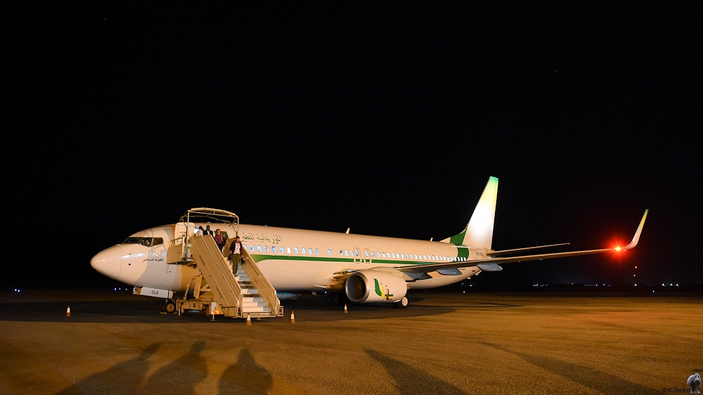 Das Bild zeigt eine weißes, zweistrahliges Passagierflugzeug mit grünem Zierstreifen auf einem nächtlichen Flughafen. Eine Treppe steht am Flieger auf der Passagiere das Flugzeug verlassen.