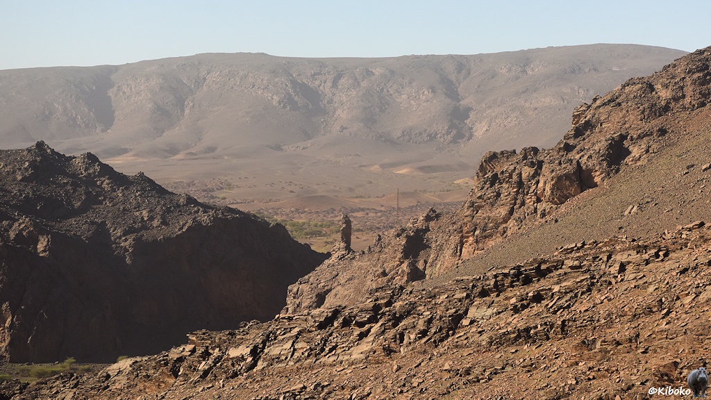 Blick in ein Tal mit Felsformationen im Vordergrund und einer weiteren Bergkette im Hintergrund.