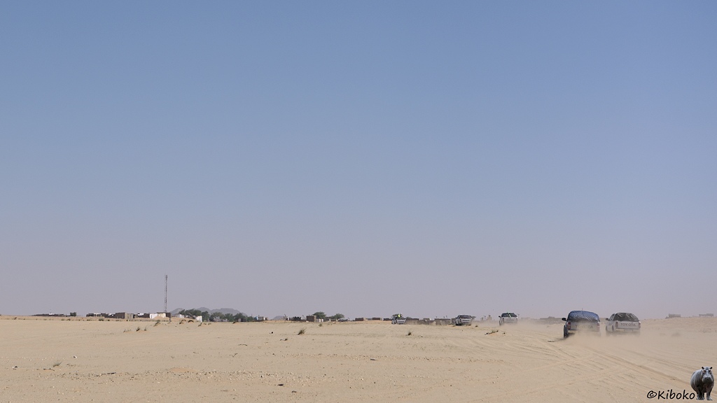 Das Bild zeigt einen Ort mit kleinen Häusern, Bäumen und einem Sendemast auf der Horizontlinie. Am rechten Bildrand fahren fünf Geländewagen auf den Ort zu.