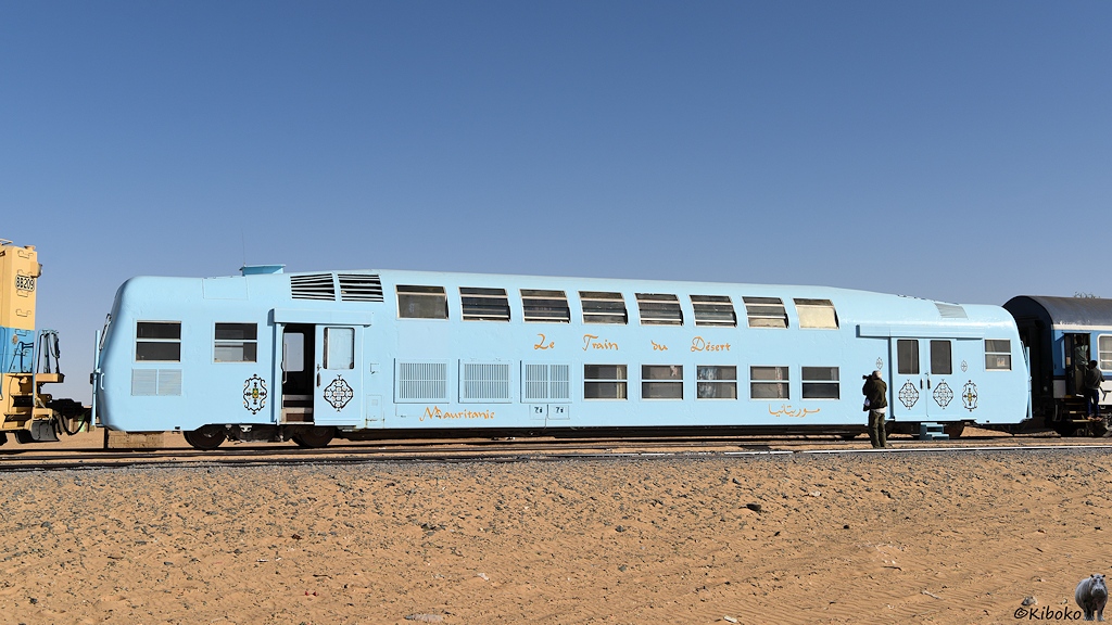 Das Bild zeigt einen doppelstöckigen, hellblauen Wagen mit doppelten Schiebetüren über den Drehgestellen. Er trägt die Anschriften Le Train Du Desert und Mauritanie.