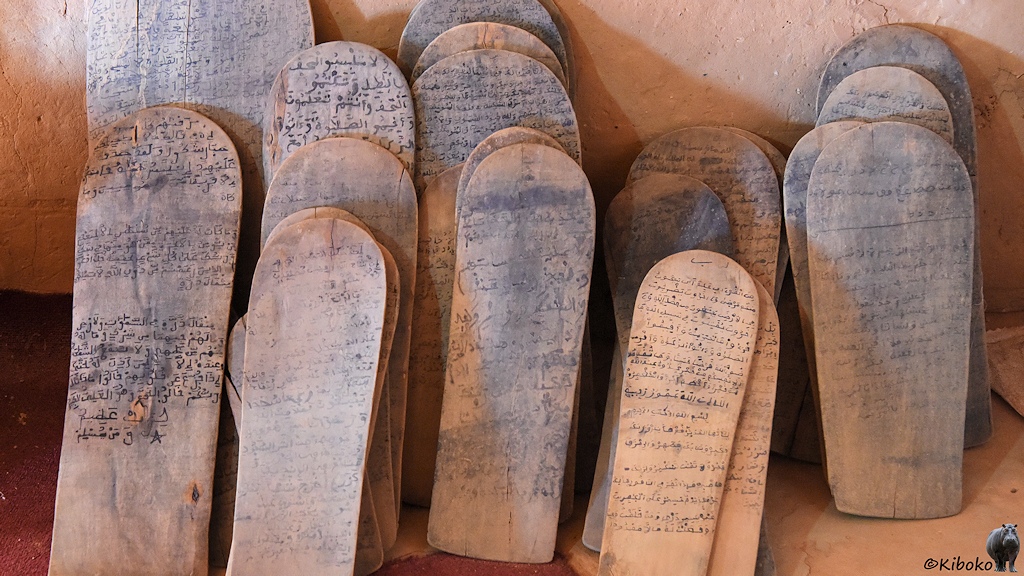 Das Bild zeigt schmale Tafeln aus Holz mit halbrunden Kopf, die an eine Wand gelehnt sind. Auf den Tafeln sind arabische Handschriften.