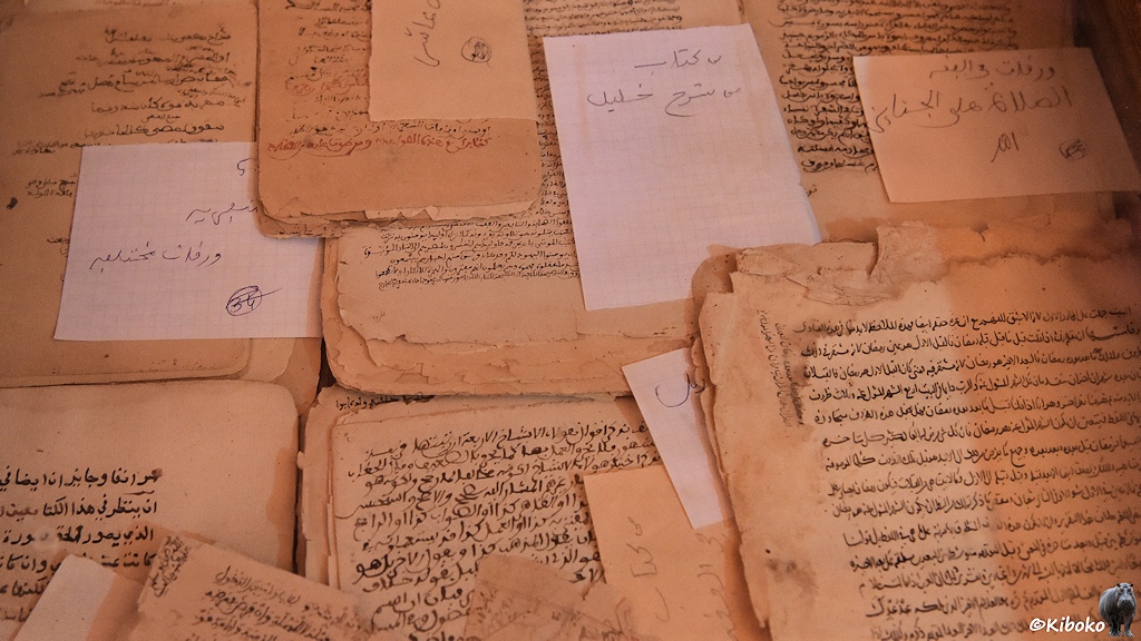 Das Bild zeigt Handschriften auf beigefarbenen Pergament und Notizen auf weißem Papier.