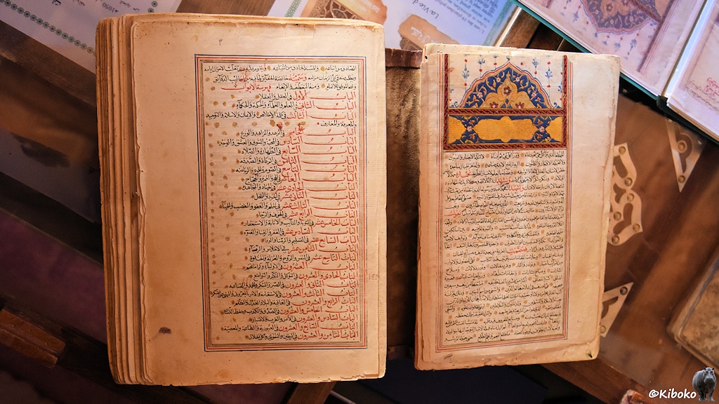 Das Bild zeigt ein altes, aufgeschlagenes Buch. Auf den beiden Seiten sind arabische Handschiften in einen kunstvollen Rahmen. Auf der rechten Seite ist im Kopf ein handgemaltes Bild mit orientalischen Mustern.