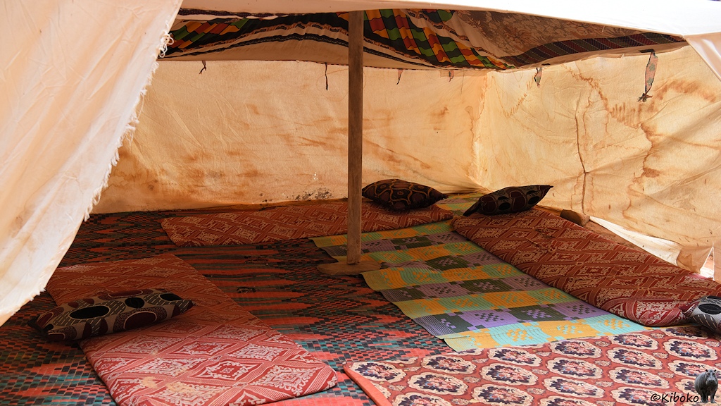 Das Bild zeigt eine Innenansicht des Zeltes. Am Rand liegen Matten mit rötlichen Mustern und Kissen.