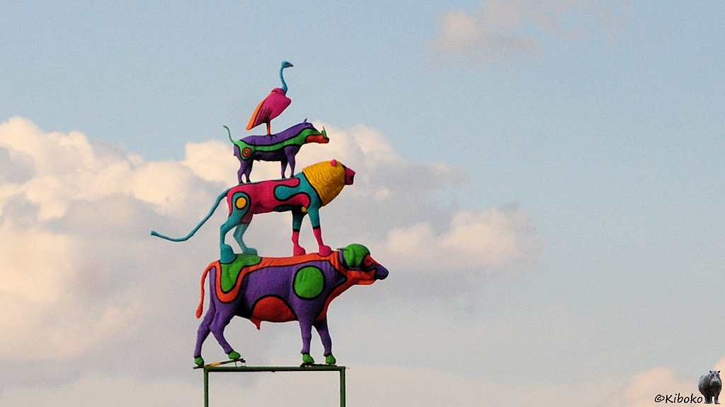 Eine Tierpyramide ähnlich den Bremer Stadtmusikanten. Auf einem Büffel steht ein Löwe, darauf ein Warzenschwein und ganz oben sitzt einn Geier. Alle Tiere sind knallbunt angemalt.