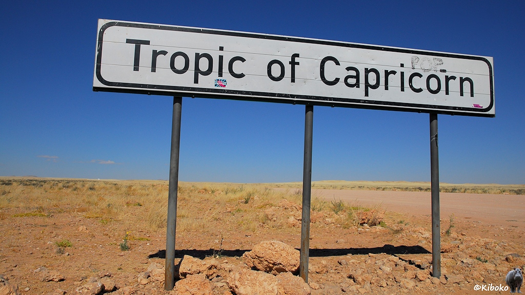 Ein Schild mit der Aufschrift Tropic of Capricon steht auf einer trockenen Grasebene.