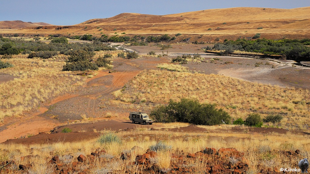 Ein Geländewagen fährt durch ein Tal. Im Hintergrund ist ein trockener Fluß und Hügel mit trockenem Gras.