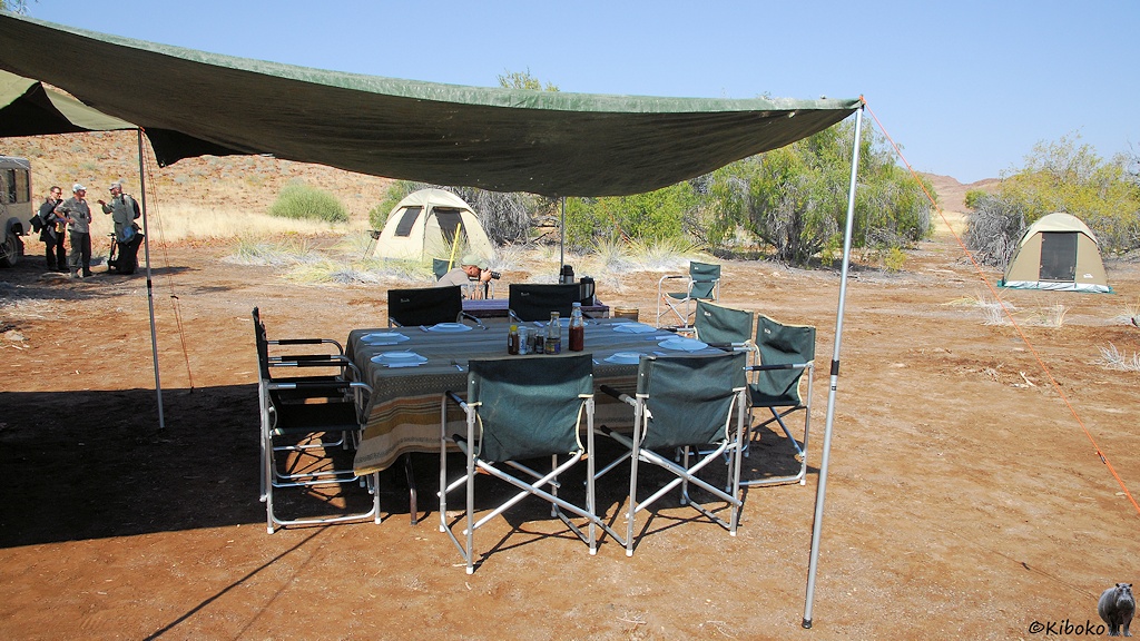Ein gedeckter Tisch mit 8 Sitzplätzen steht unter einem Zeltdach. Im Hintergrund stehen kleine Kuppelzelte.