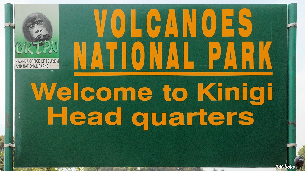 Das Bild zeigt ein grünes Blechschild mit grüner Schirft: Volcanoes National Park - Welcome to Kinigi Headquarters